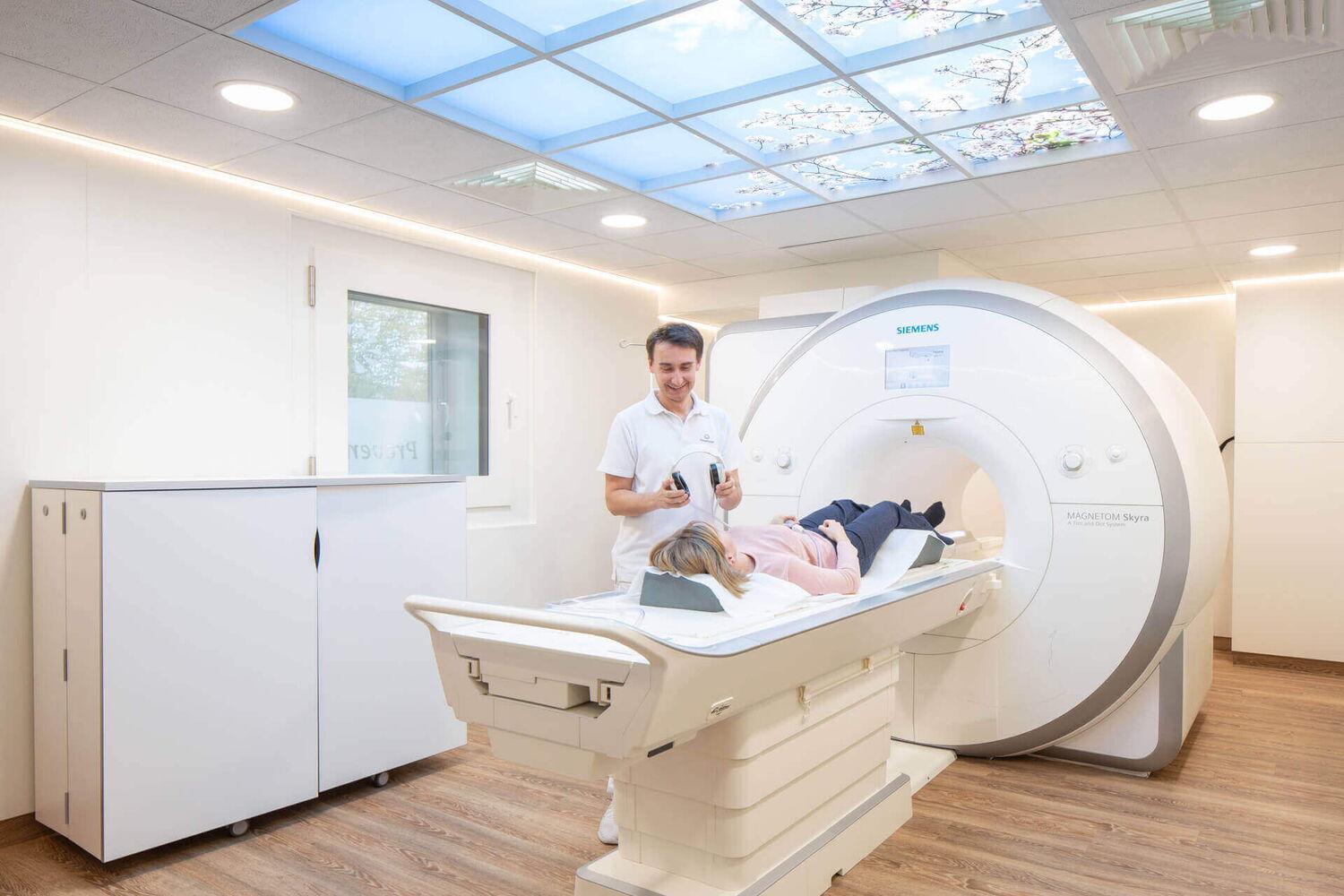 Vorbereitung der 3-Tesla MRT Untersuchung im Metamedicum in Essen. Ein kompetenter medizinischer Mitarbeiter setzt der entspannten Patientin Kopfhörer für eine angenehme radiologische Untersuchung auf.